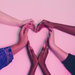 A group of diverse hands forming a heart shape against a soft pink background, symbolizing love and unity.